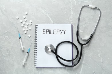 Photo of Notebook with word Epilepsy, stethoscope, pills and syringes on grey marble table, flat lay