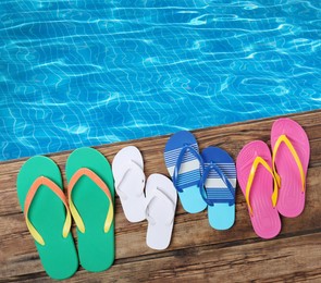 Image of Pairs of flip flops on wooden deck near swimming pool, flat lay 