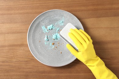 Woman washing dirty plate at wooden table, top view