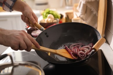 Photo of Man stirring onion slices in frying pan, closeup