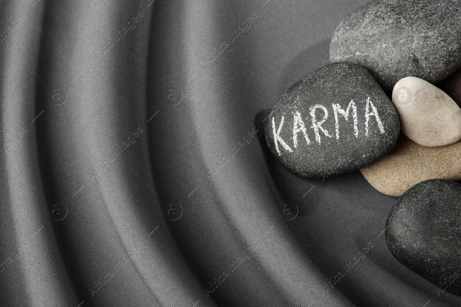 Photo of Stones with word Karma on grey fabric, above view. Space for text