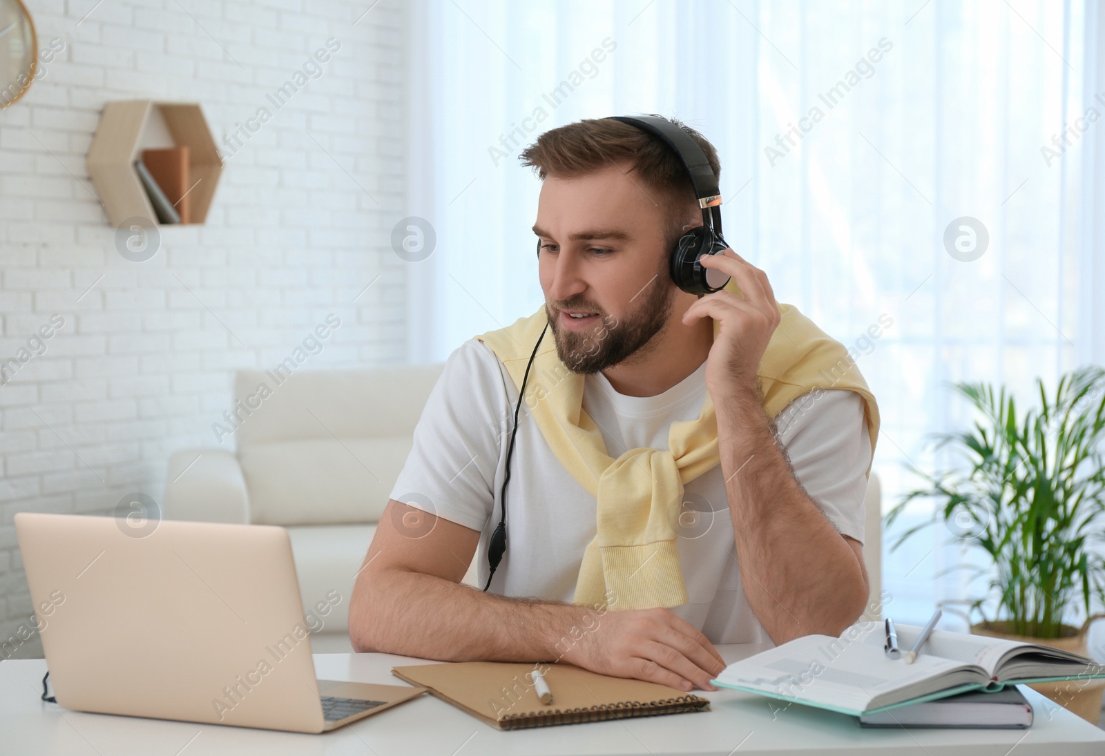 Photo of Young man watching online webinar at table indoors