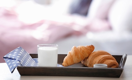 Wooden tray with tasty croissants and glass of milk on table