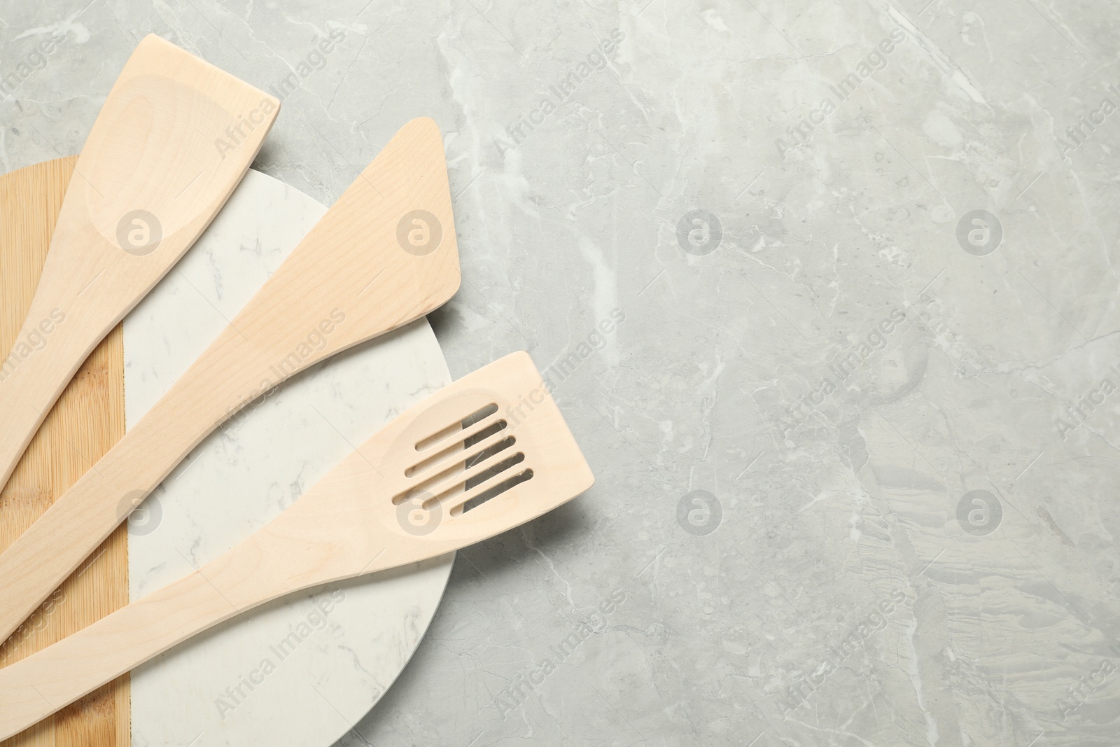 Photo of Different wooden spatulas and board on grey textured table, top view. Space for text