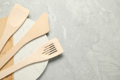 Photo of Different wooden spatulas and board on grey textured table, top view. Space for text