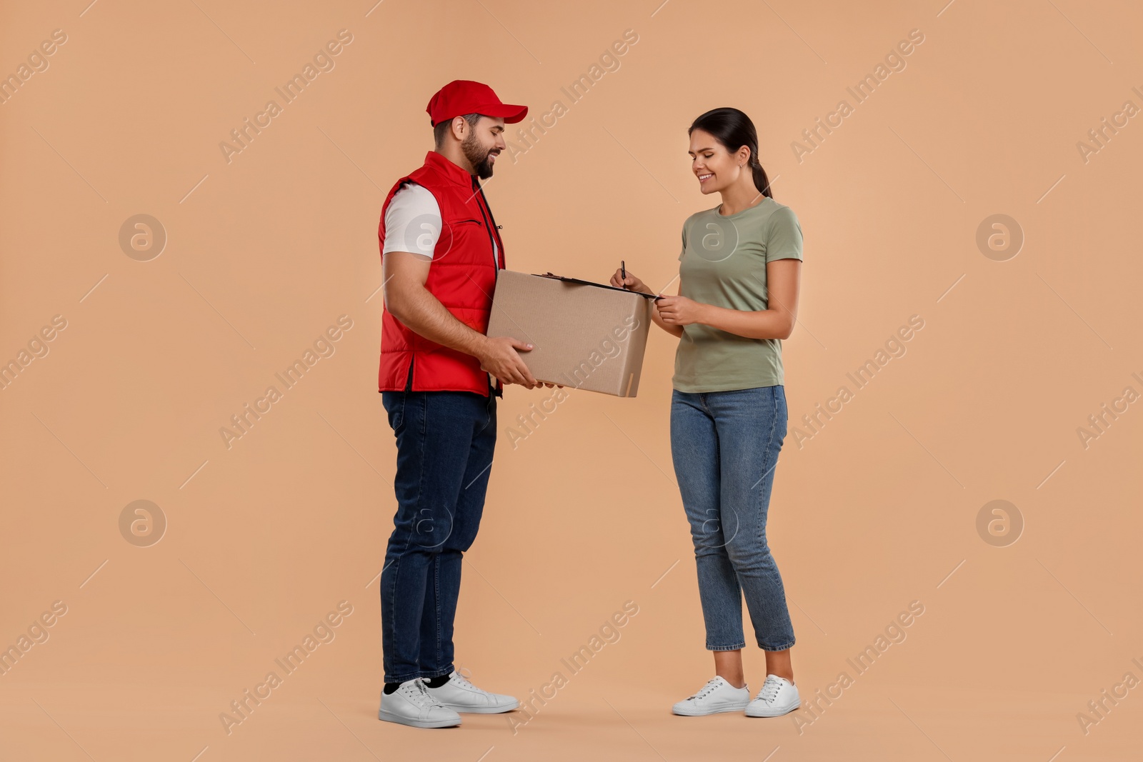 Photo of Smiling woman signing order receipt on light brown background. Courier delivery