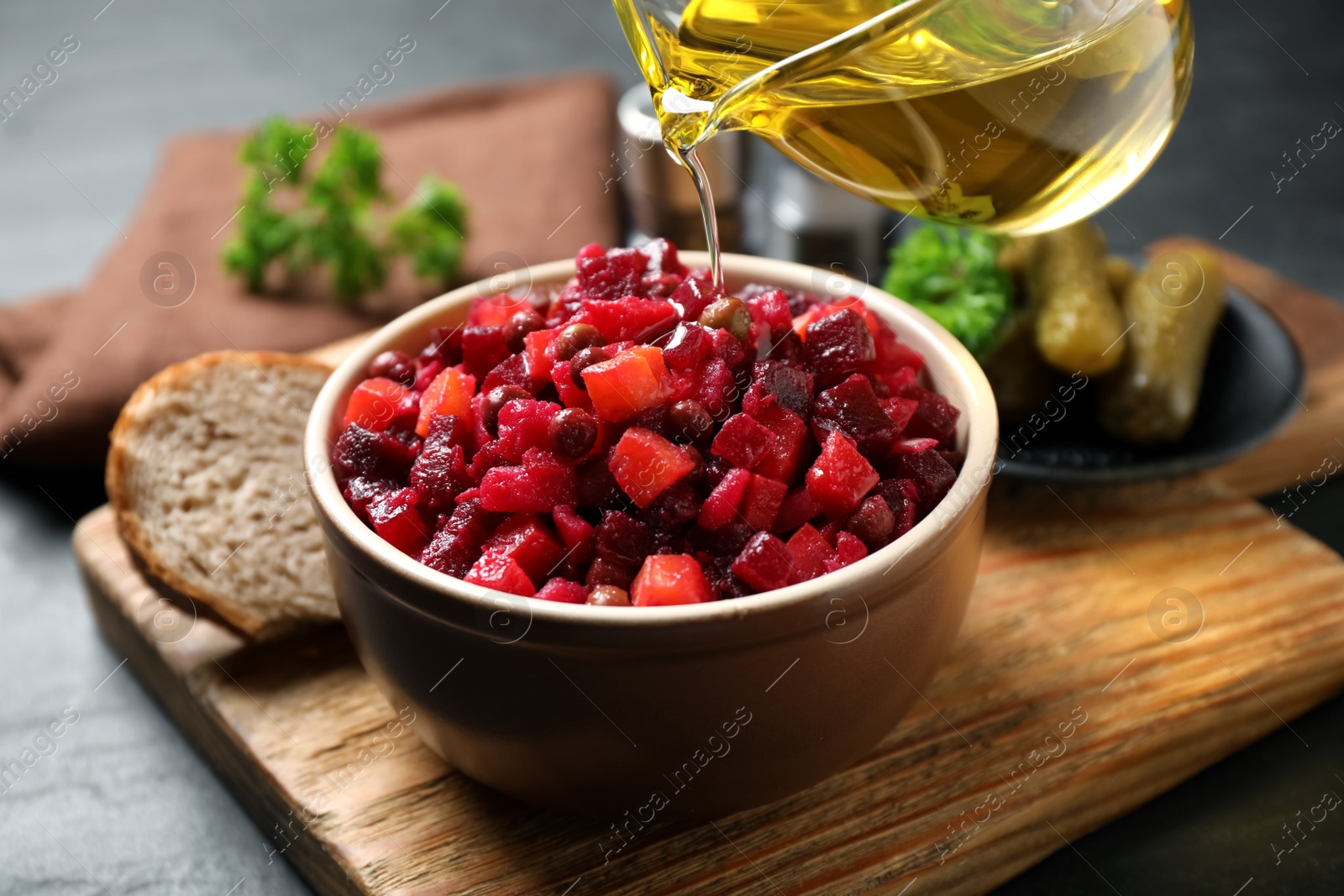 Photo of Adding oil to traditional Russian salad vinaigrette on wooden board, closeup