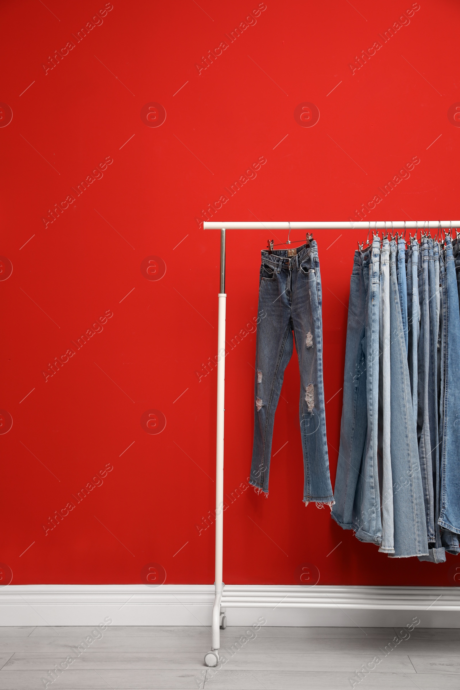 Photo of Rack with stylish jeans near red wall