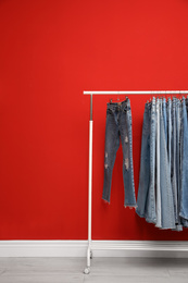 Photo of Rack with stylish jeans near red wall
