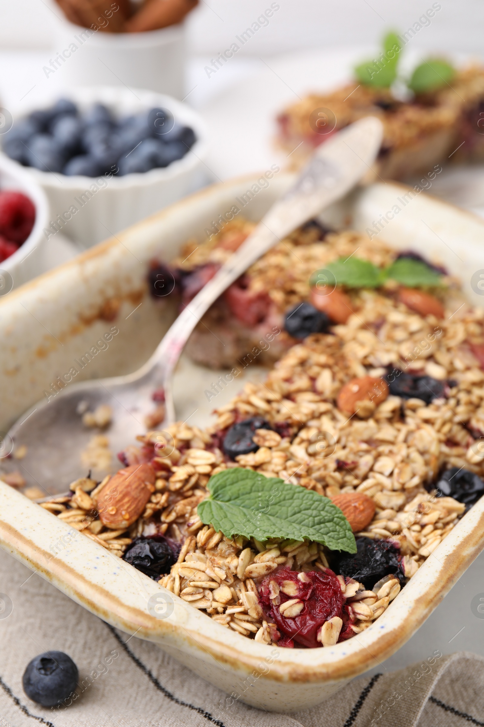 Photo of Tasty baked oatmeal with berries and almonds in baking tray on table, closeup