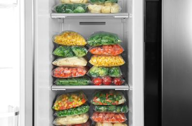 Plastic bags with different frozen vegetables in refrigerator