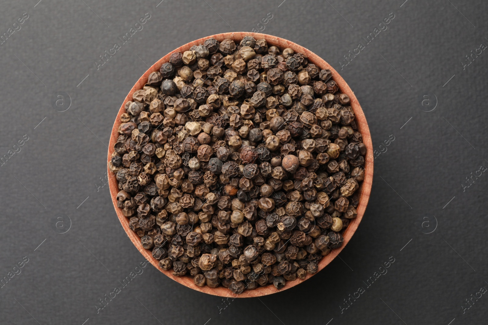 Photo of Bowl of spicy black pepper grains on grey background, top view