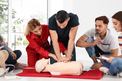 Photo of Group of people with instructor practicing CPR on mannequin at first aid class indoors