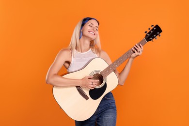 Photo of Happy hippie woman playing guitar on orange background
