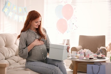Happy pregnant woman with gift box in room decorated for baby shower party
