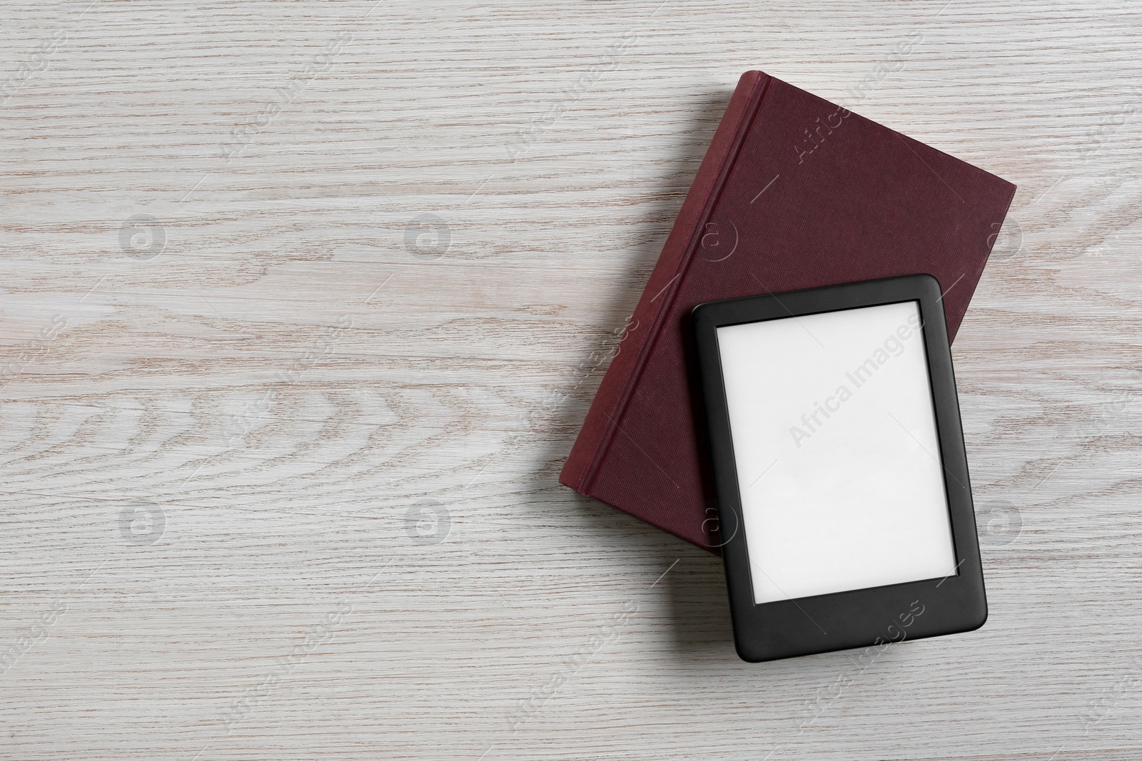 Photo of Portable e-book reader and hardcover book on white wooden table, top view. Space for text