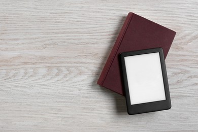 Photo of Portable e-book reader and hardcover book on white wooden table, top view. Space for text