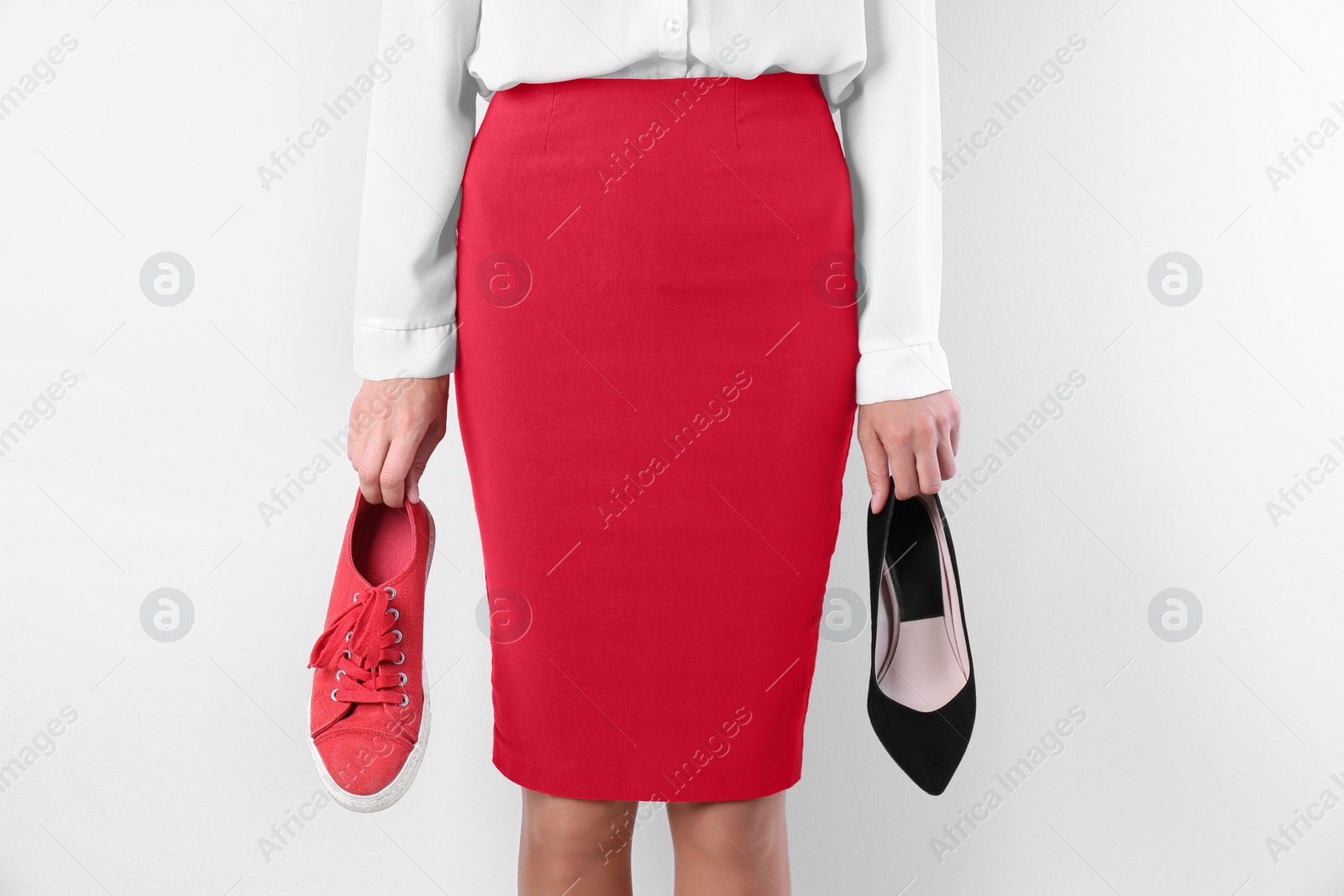 Photo of Woman holding high heeled shoe and sneaker on white background, closeup. Choice concept