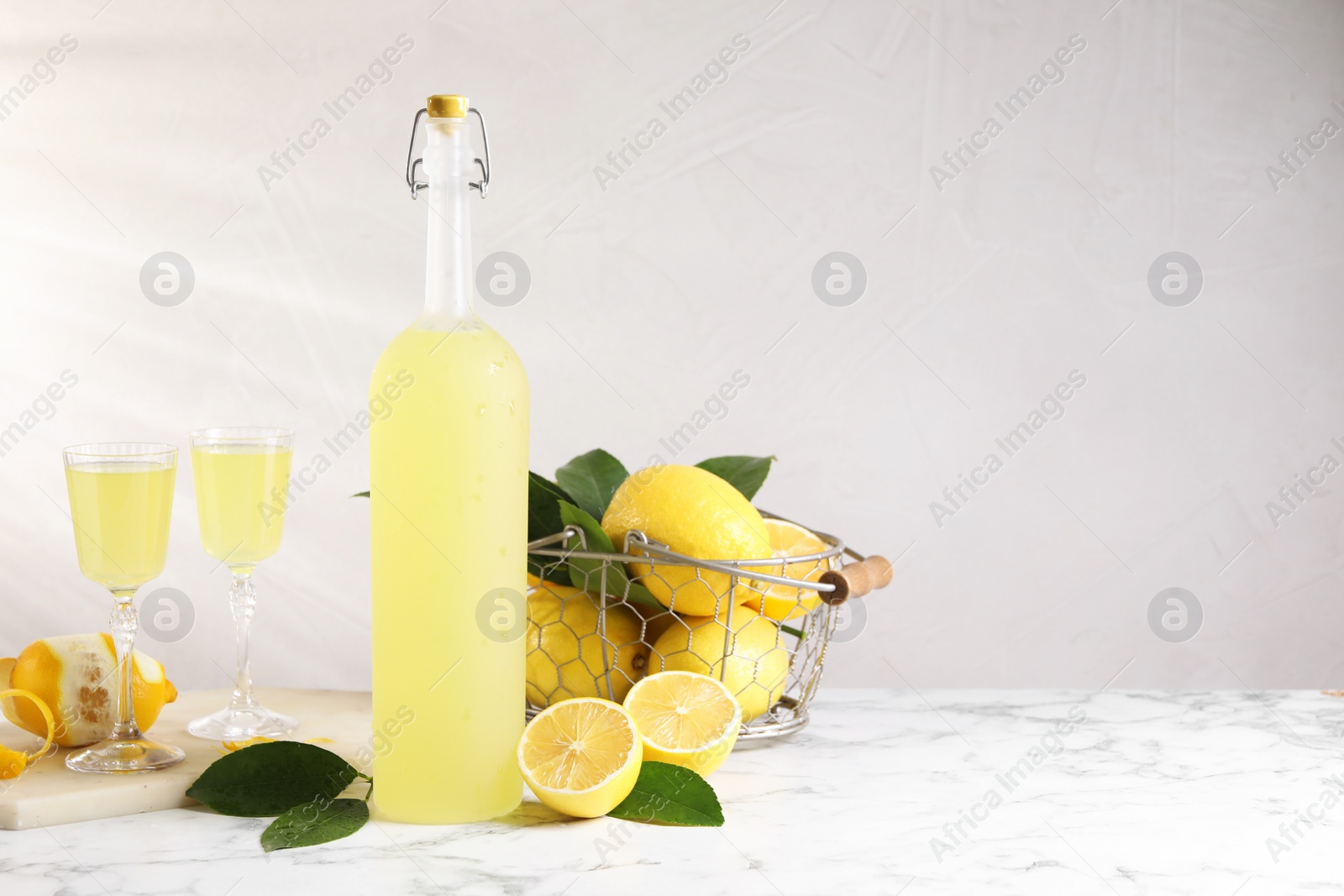 Photo of Tasty limoncello liqueur, lemons and green leaves on white marble table, space for text