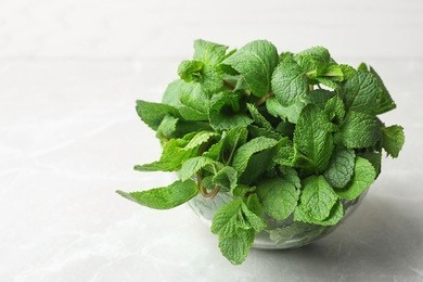 Glass bowl full of fresh green mint on light background, space for text