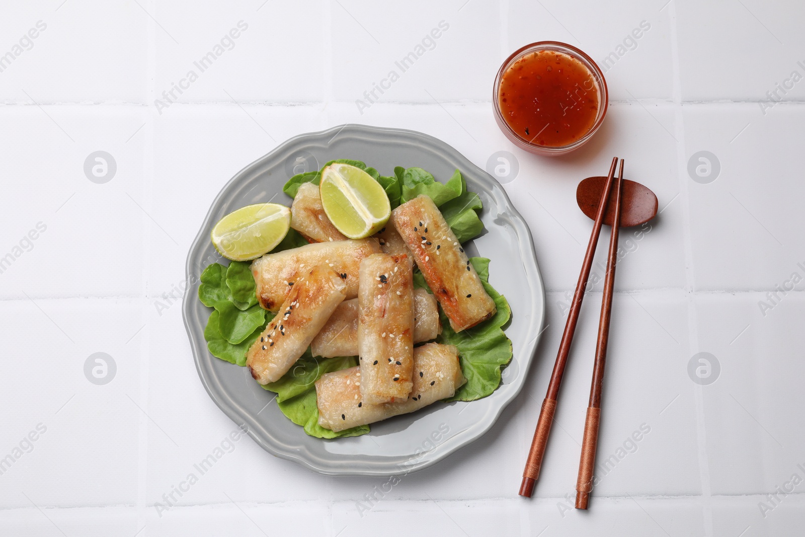 Photo of Tasty fried spring rolls served on white tiled table, flat lay