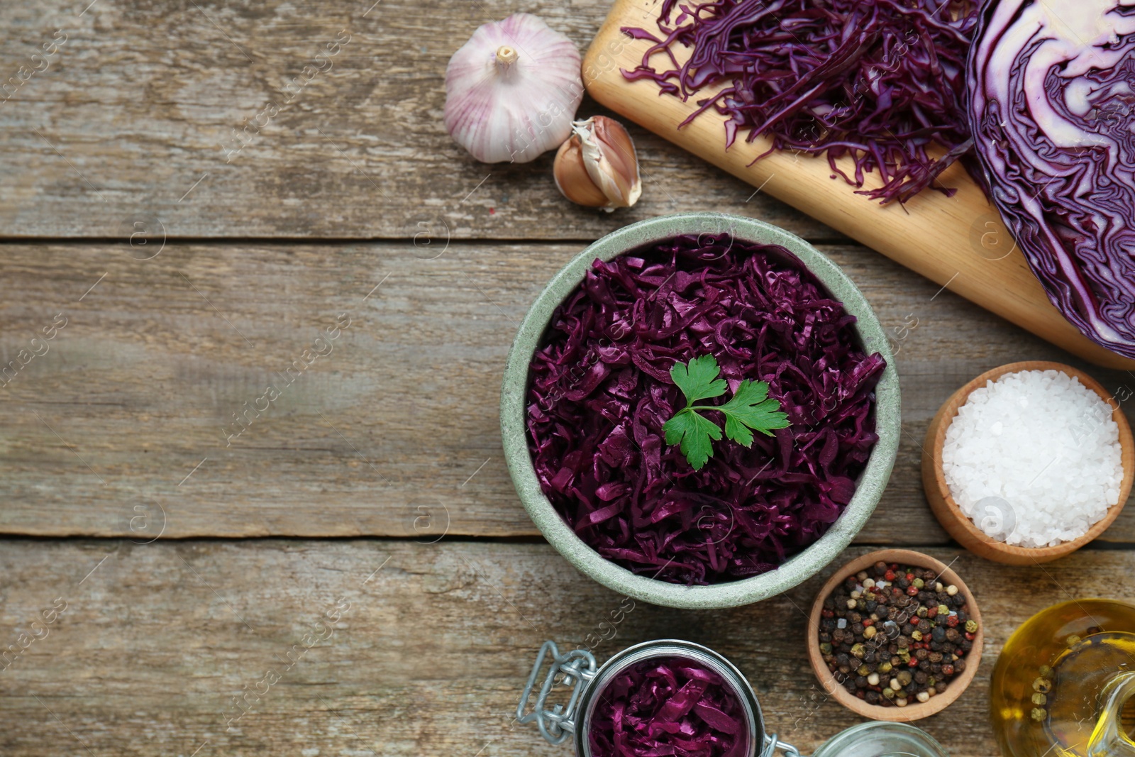 Photo of Tasty red cabbage sauerkraut with parsley and different ingredients on wooden table, flat lay. Space for text