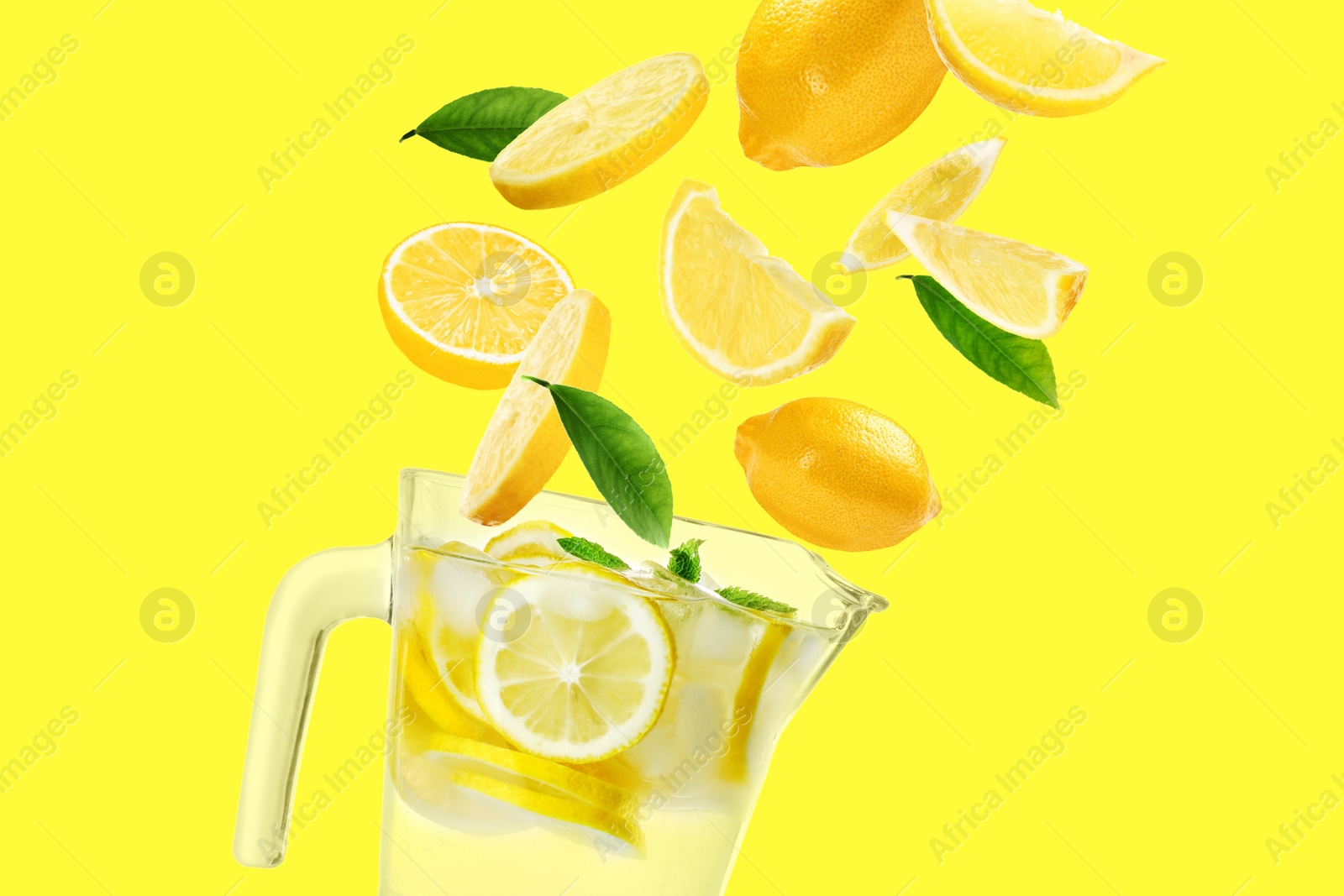 Image of Glass jug with natural lemonade, fruits and green leaves flying on yellow background