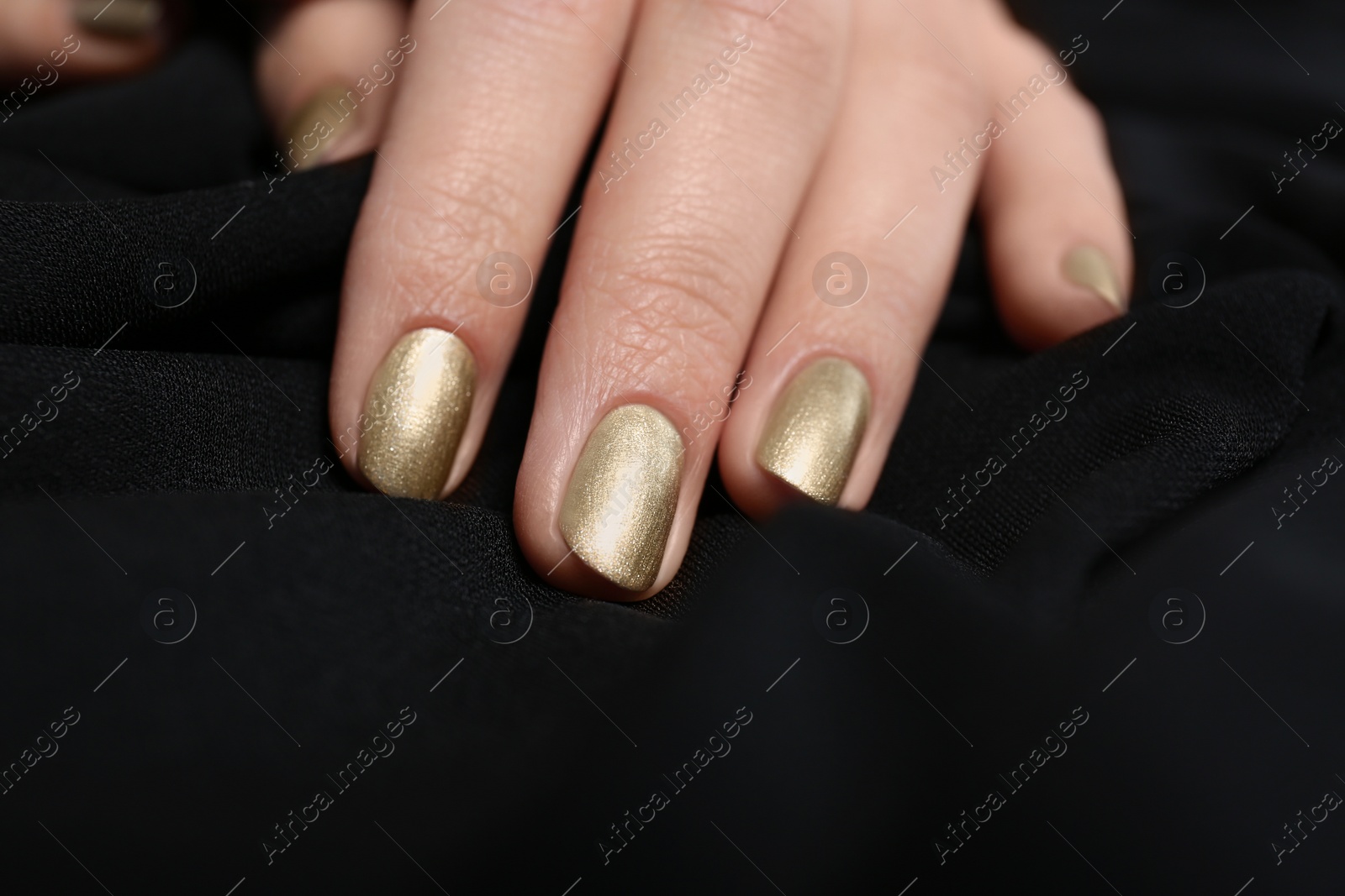 Photo of Woman with golden manicure on black fabric, closeup. Nail polish trends