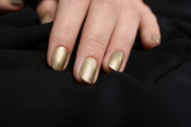 Photo of Woman with golden manicure on black fabric, closeup. Nail polish trends