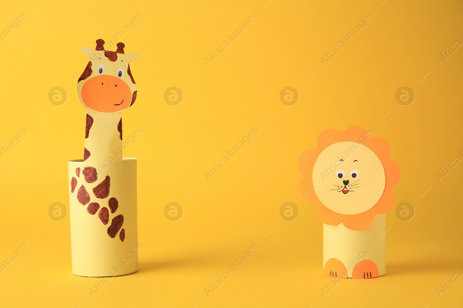 Photo of Toy giraffe and lion made from toilet paper hubs on yellow background, space for text. Children's handmade ideas