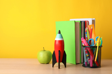 Bright toy rocket and school supplies on wooden table. Space for text