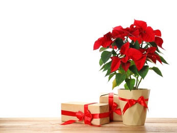 Red Poinsettia in pot and gifts on wooden table, space for text. Christmas traditional flower