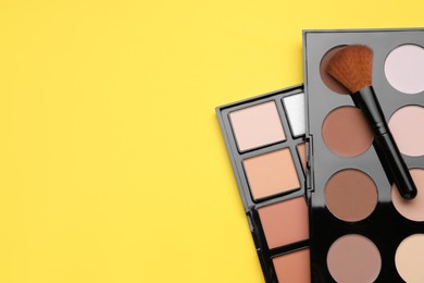 Different contouring palettes and brush on yellow background, flat lay with space for text. Professional cosmetic product