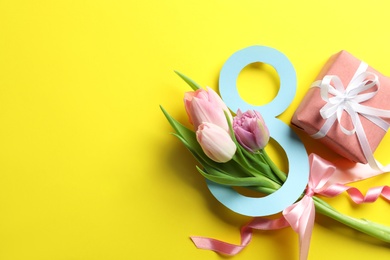 Photo of 8 March card design with tulips, gift and space for text on yellow background, flat lay. International Women's Day