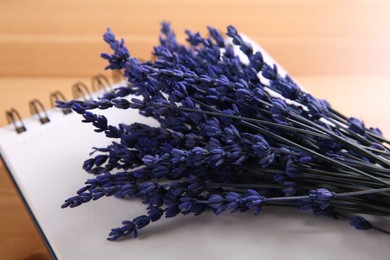 Photo of Bouquet of beautiful preserved lavender flowers and notebook on wooden table, closeup