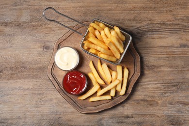 Photo of Tasty French fries served with sauces on wooden table, top view