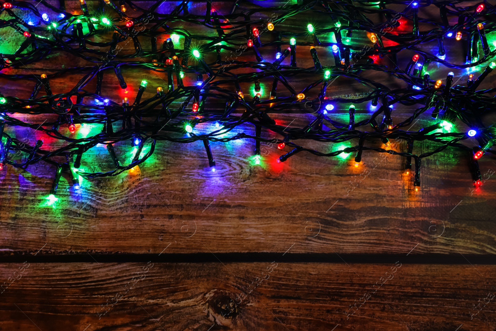 Photo of Glowing festive lights on wooden table, top view. Space for text