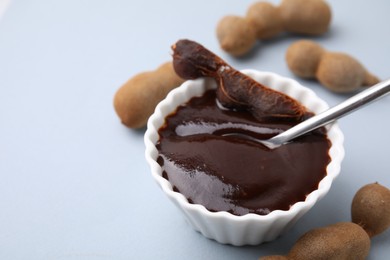 Photo of Bowl of tamarind sauce, spoon and fresh pods on light grey table, closeup. Space for text