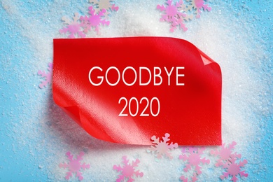 Text Goodbye 2020 and artificial snow on light blue background, flat lay