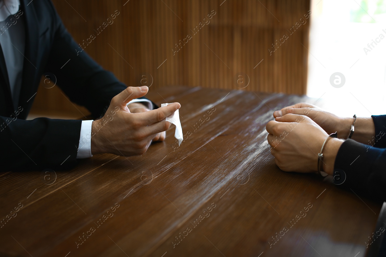 Photo of Police officer interrogating drug dealer in handcuffs at desk indoors. Criminal law