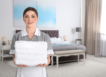 Beautiful chambermaid with clean folded towels near bed in hotel room