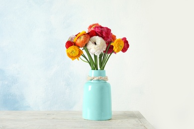 Photo of Vase with beautiful ranunculus flowers on table against color background