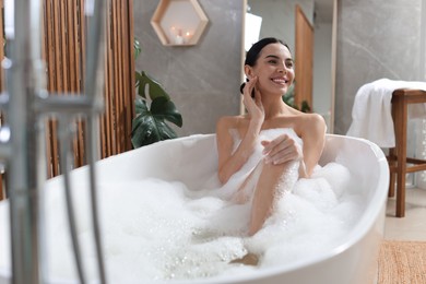 Beautiful young woman taking bubble bath at home