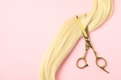 Professional hairdresser scissors with blonde hair strand on pink background, top view. Space for text