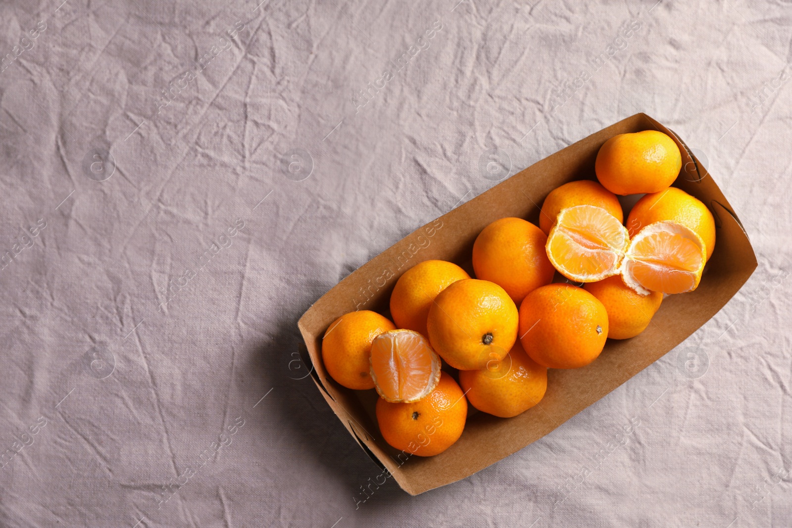 Photo of Paper box with fresh ripe tangerines on beige cloth, top view. Space for text