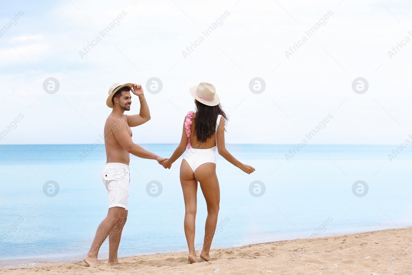 Photo of happy young couple walking together on beach near sea. Space for text