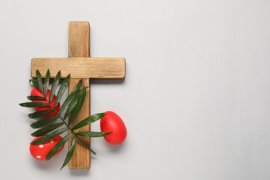 Wooden cross, painted Easter eggs and palm leaf on light grey background, flat lay. Space for text