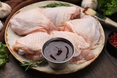 Plate with fresh marinade, raw chicken and rosemary on wooden table, closeup