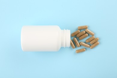 Bottle and vitamin capsules on light blue background, top view