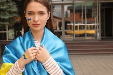 Young woman with Ukrainian flag outdoors, space for text